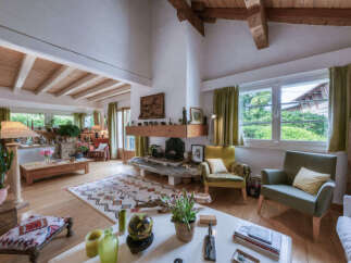 This spacious living room boasts a charming rustic aesthetic with exposed wooden beams and a prominent stone fireplace.