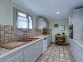 This charming kitchen features a double basin sink and a light-colored countertop, complemented by a tiled backsplash and white cabinetry.