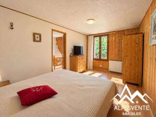 This charming bedroom features a comfortable bed with a decorative red pillow, a wooden dresser with a television, and a large wardrobe.