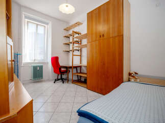 This cozy bedroom features a large wooden wardrobe, a functional desk area with a red office chair, and a comfortable bed.