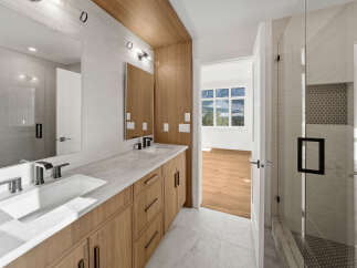 This modern bathroom features a sleek double vanity with a marble countertop and warm wood cabinetry, complemented by minimalist black fixtures.