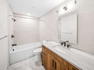 This modern bathroom features a sleek design with a white bathtub and toilet, complemented by a spacious vanity with a marble countertop and wooden cabinetry.