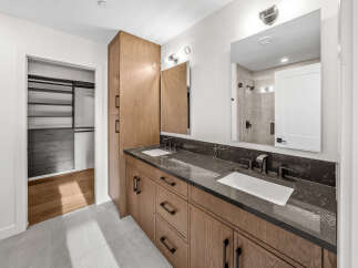 This modern bathroom features a spacious double vanity with a dark, veined countertop and warm wood cabinetry.