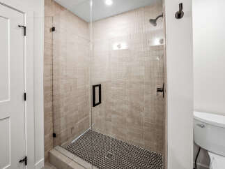 Step into a beautifully designed bathroom featuring a spacious glass-enclosed shower with elegant tile work and a modern black handle.