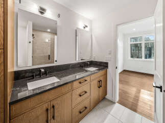 Experience modern luxury in this stunning bathroom featuring a spacious double vanity with a sleek, dark stone countertop and warm wood cabinetry.