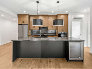 This modern kitchen boasts sleek, dark cabinetry on the island, complemented by a stunning marble countertop.