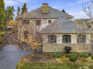 This stunning home boasts a beautiful stone facade and a grand pitched roof, complemented by a prominent stone chimney.