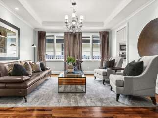 Experience luxurious living in this elegantly appointed living room, featuring a plush brown leather sofa adorned with decorative pillows and a sleek glass-top coffee table.