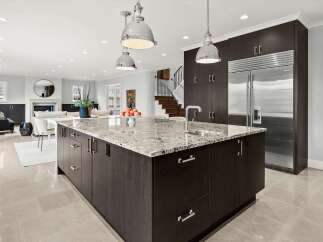 This spacious open-concept kitchen boasts dark wood cabinetry and a large granite-topped island with a built-in sink and faucet.