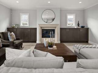 This elegant living room features a modern fireplace with a large circular mirror above, flanked by built-in dark wood cabinets.
