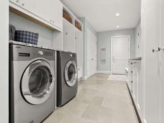This spacious laundry room boasts a modern aesthetic with sleek Asko washer and dryer units, complemented by granite countertops and ample white cabinetry for storage.