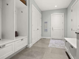 This spacious mudroom features a built-in white bench with ample storage drawers and a convenient cubby system with hooks for coats and bags.