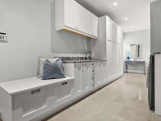 This spacious laundry room boasts ample white cabinetry for storage, complemented by a granite countertop and a stainless steel sink.