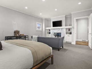 Experience luxury and comfort in this spacious master suite, featuring a cozy seating area with a fireplace and a wall-mounted TV.