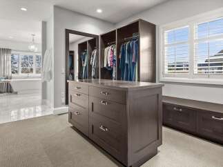 Step into this luxurious walk-in closet, featuring a spacious island with ample drawer storage and a built-in bench with additional cabinets.