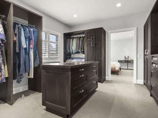 Step into this spacious walk-in closet, featuring custom dark wood cabinetry and ample hanging space for both suits and casual wear.