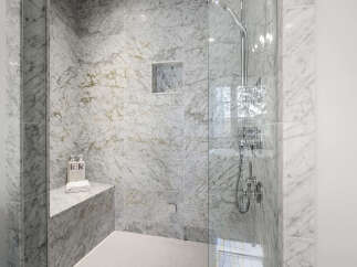 Indulge in luxury with this stunning marble-clad shower, featuring a built-in bench and a sleek glass enclosure.