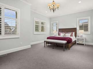 This spacious bedroom features a comfortable king-size bed with a rich burgundy comforter and plush pillows, complemented by a white upholstered bench at the foot of the bed.
