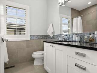 This modern bathroom features a sleek white vanity with a black countertop, complemented by a decorative mosaic tile backsplash.