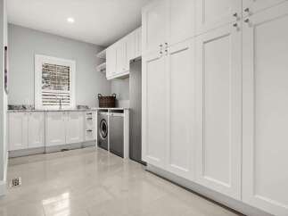 This spacious laundry room boasts ample storage with floor-to-ceiling white cabinets and a convenient countertop space.