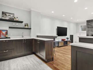 This modern basement features a sleek wet bar with dark wood cabinetry, white countertops, and a stainless steel sink, perfect for entertaining.
