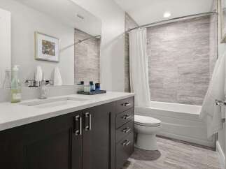 This modern bathroom features a sleek dark wood vanity with a white quartz countertop and a undermount sink.