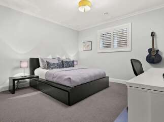 This modern bedroom features a stylish dark wood platform bed with integrated storage, complemented by a sleek bedside table and a contemporary lamp.