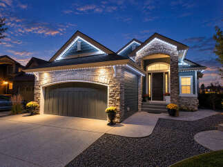 This stunning home boasts a beautiful stone and siding exterior, illuminated by elegant string lights that highlight its architectural details.