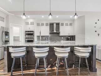 This modern kitchen boasts a sleek stainless steel refrigerator and a matching range hood, complemented by white cabinetry and a granite-topped island.