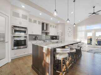 Experience luxury in this stunning modern kitchen, featuring sleek white cabinetry, a spacious granite island with bar seating, and top-of-the-line stainless steel appliances including double ovens and a microwave.