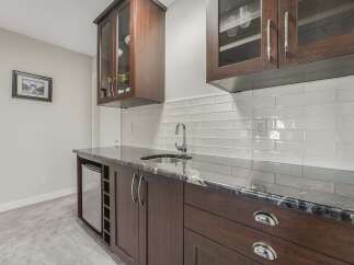 This modern wet bar features dark wood cabinetry with glass-front upper cabinets, perfect for displaying glassware.