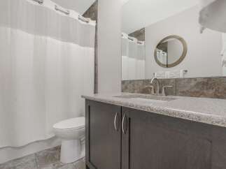 This modern bathroom features a sleek vanity with a granite countertop and a brushed nickel faucet, complemented by a large mirror with a decorative frame.