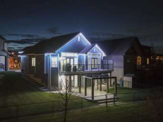 This stunning modern home features a beautiful blue exterior, illuminated by festive white lights along the roofline.
