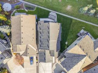 Experience luxury living in this stunning aerial view of a multi-level home featuring a complex roofline with both light and dark shingles.