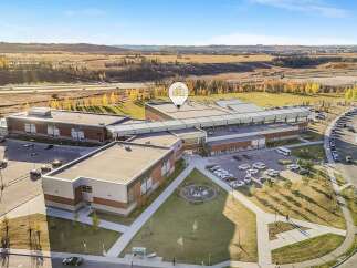 This aerial view showcases a modern educational facility with expansive grounds, featuring ample parking and sports fields.