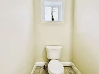 This bathroom features a clean white toilet situated in a corner, complemented by neutral-toned walls and tiled flooring.