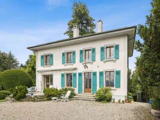 This charming white house boasts vibrant teal shutters on its numerous windows, adding a pop of color to the facade.