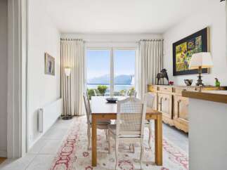 Enjoy breathtaking lake and mountain views from this elegant dining room, featuring a large wooden table set for four and a charming buffet.