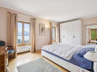 Experience serene lakeside living in this beautifully appointed bedroom, featuring expansive windows that offer breathtaking views of the water and mountains.