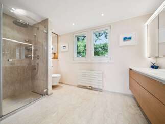 Experience modern luxury in this spacious bathroom, featuring a sleek glass-enclosed shower with marble-look tiles and a rainfall showerhead.