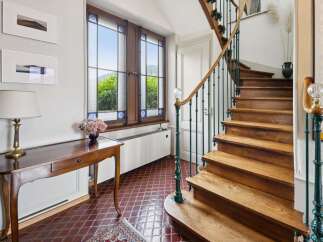 Step into this charming entryway featuring a beautiful wooden staircase with ornate green railings and a crystal newel post.
