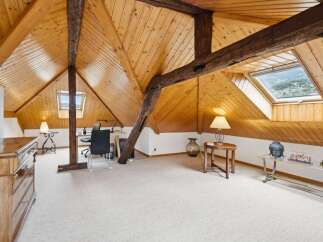 Discover this charming attic office space, featuring a warm wooden ceiling with exposed beams and a skylight offering scenic views.