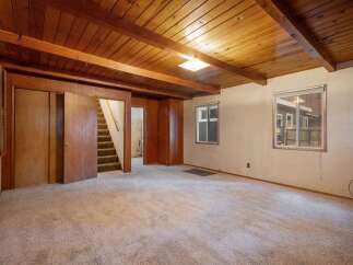 Step into this cozy living space featuring a warm, wood-paneled ceiling with exposed beams and a plush carpeted floor.