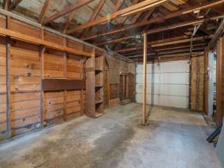 This spacious garage offers ample storage and workspace, featuring durable wooden walls and shelving units.