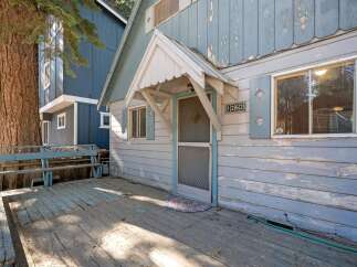 This charming property features a weathered blue exterior with a welcoming front porch and a rustic wooden deck.