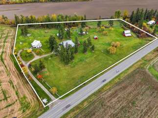 Discover this expansive rural property featuring a charming white farmhouse and a classic red barn, perfect for a serene country lifestyle.