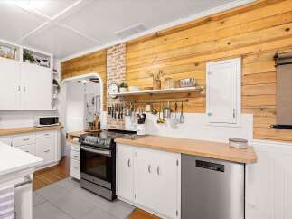 This charming kitchen boasts a rustic yet modern aesthetic, featuring warm wooden plank walls that complement the crisp white cabinetry and subway tile backsplash.