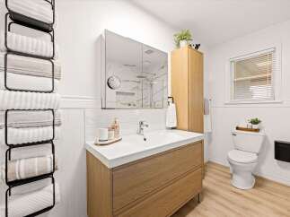 This modern bathroom features a sleek wooden vanity with a white countertop and a large undermount sink.