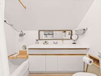 This charming bathroom features a sleek white vanity with wood accents, complemented by a long rectangular mirror reflecting a glimpse of the kitchen.