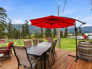 Enjoy outdoor dining and relaxation on this spacious wooden deck, complete with a large table and chairs under a vibrant red umbrella.